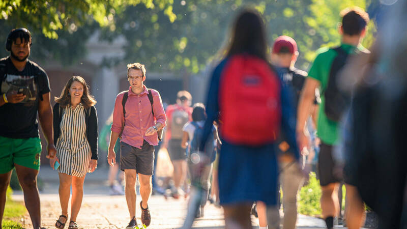 Students and staff walk on a South Quad sidewalk during sunny day