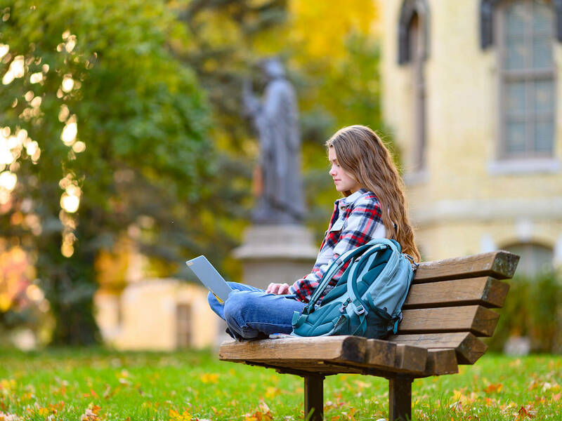 Student working with laptop on a bench during a fall day on campus